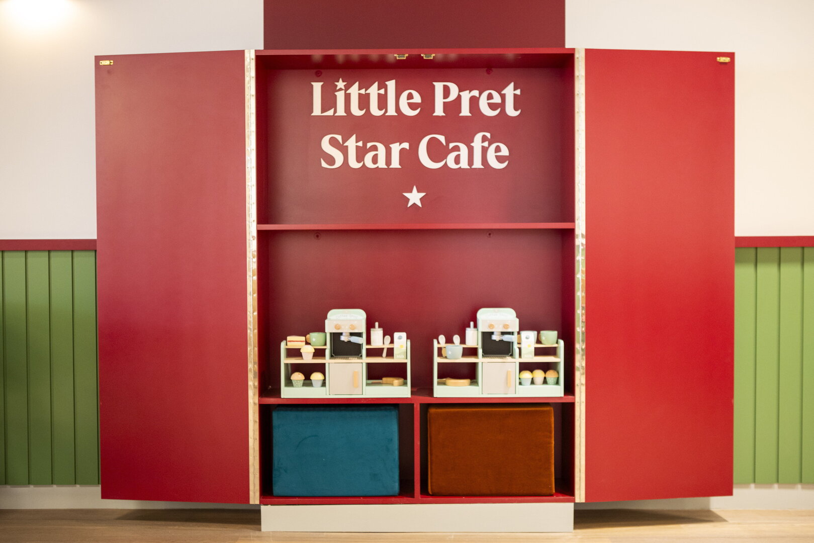 Red cabinet with 'little pret star cafe' sign and children play kitchen inside.