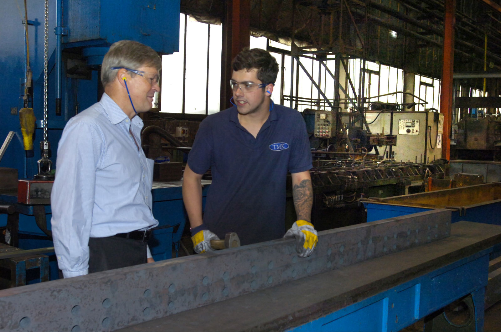 Managing director and apprentice examining a metal beam in a factory.